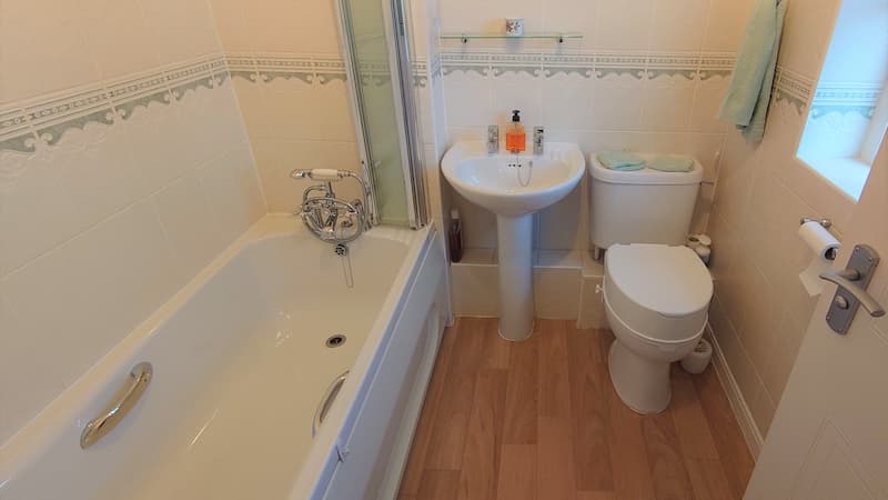 bathroom with bath, screen, toilet and sink with wooden flooring