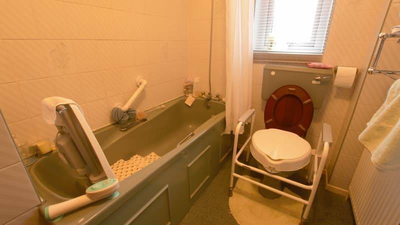 Bathroom with bath, handrails, shower curtain and supported toilet